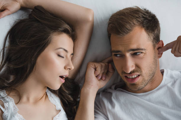 top view of man closing ears and looking at snoring wife in bed stock photo
