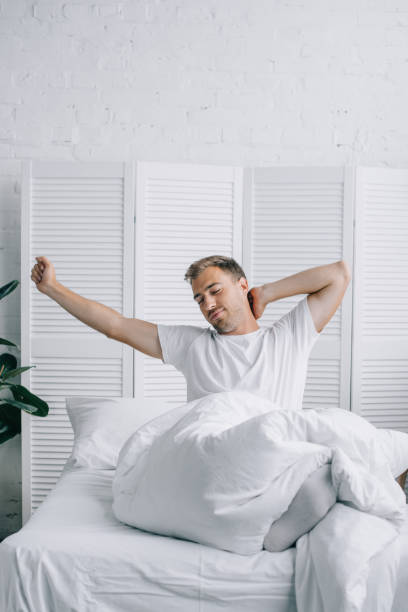 istock handsome young man sitting on bed and stretching at morning 1020527288