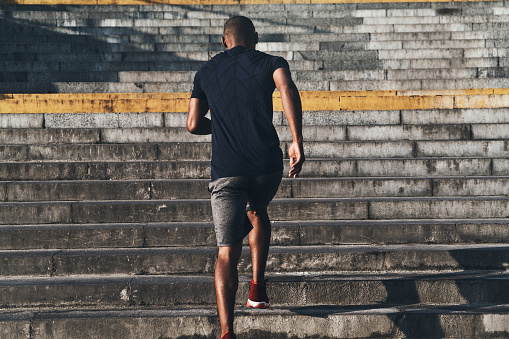 Rear view of young African man in sports clothing running up the stairs while exercising outdoors