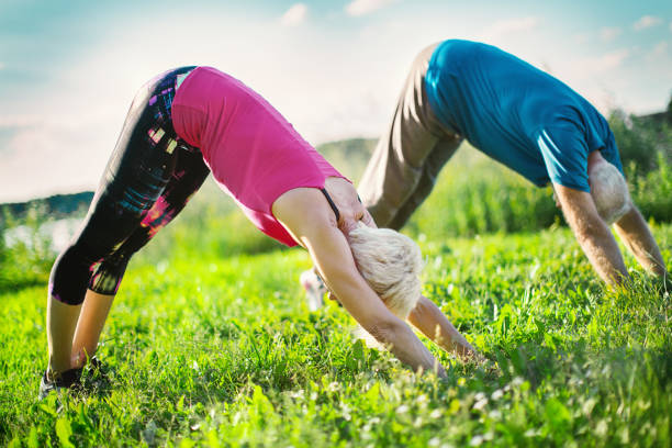 Senior Yoga. Mature couple in downward facing dog position outdoors. Side view. Horizontal. downward facing dog position stock pictures, royalty-free photos & images
