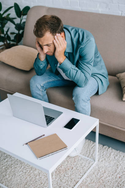 istock high angle view of young man with headache using laptop at home 1020548320