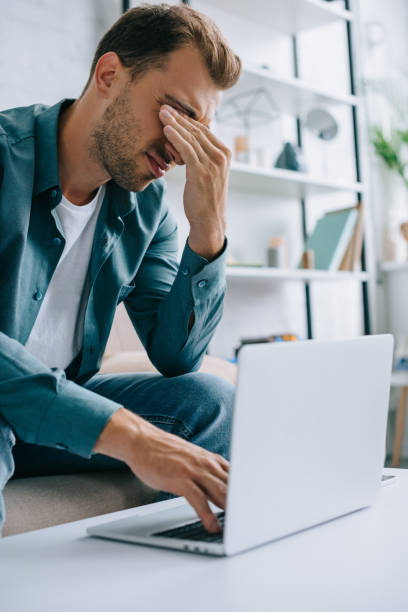 istock young man with pain in eyes and headache using laptop at home 1020548364