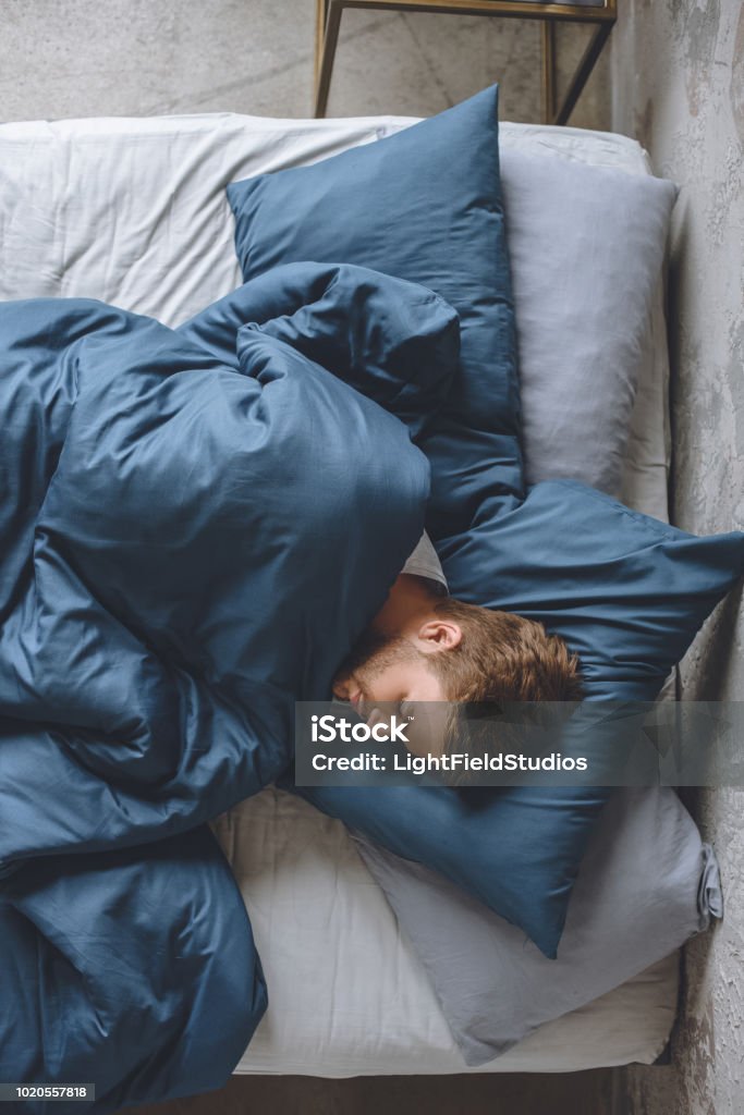 top view of young handsome man sleeping under blanket in his bed at home Sleeping Stock Photo