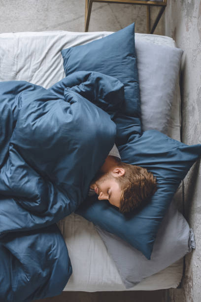 top view of young handsome man sleeping under blanket in his bed at home top view of young handsome man sleeping under blanket in his bed at home man sleeping on bed stock pictures, royalty-free photos & images