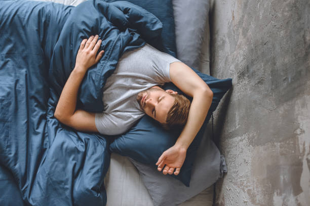 istock elevated view of young handsome man sleeping under blanket in his bed at home 1020557828
