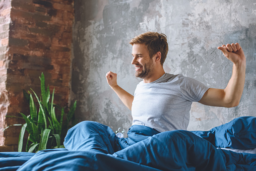 handsome young man stretching in bed during morning time at home