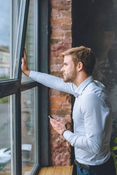 istock pensive young businessman with smartphone looking in windows at home 1020561886