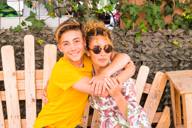 mère et fils étreindre avec sourire et profiter de temps libre ainsi que de l’amour. famille adolescent garçon âgé de 14 ans et maman 43 amusez-vous assis sur un banc en bois en plein air - nature sitting 13 14 years cute photos et images de collection