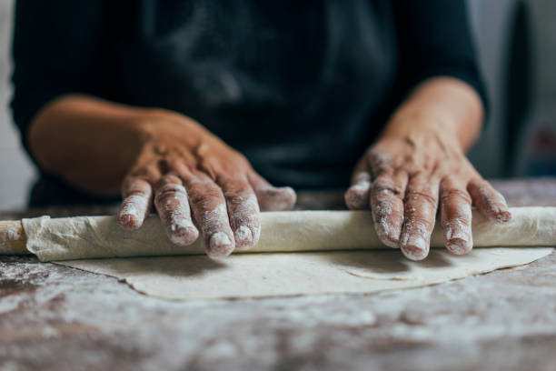 istock Close up of woman's hands stretching dough with rolling pin on kitchen counter 1020586046