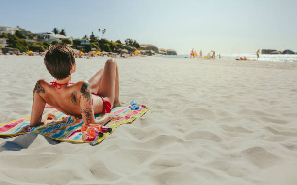 Woman in swimsuit sitting on a towel sunbathing at the beach. Woman on vacation relaxing at the beach on a sunny day.
