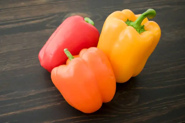 Red, orange, and yellow bell peppers on a wooden cutting board