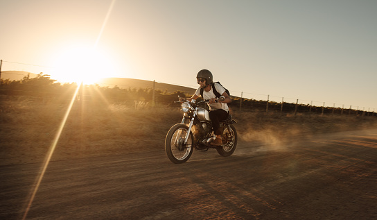 Male biker driving a vintage motorcycle on dirt road. Man riding fast on his bike on countryside road.