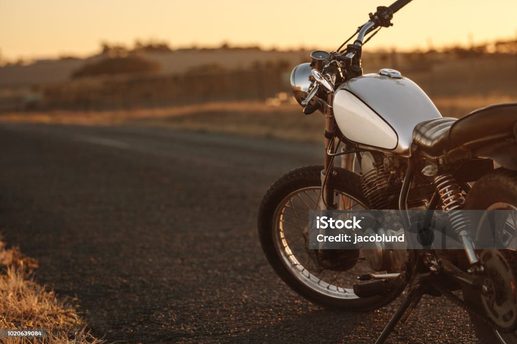 Vintage motorcycle on country road Vintage motorcycle parked on empty country road. Vintage motorbike standing at the side of the road in evening. Motorcycle Stock Photo