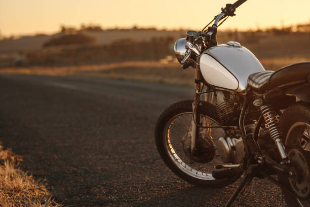 Vintage motorcycle on country road Vintage motorcycle parked on empty country road. Vintage motorbike standing at the side of the road in evening. motorcycle photos stock pictures, royalty-free photos & images