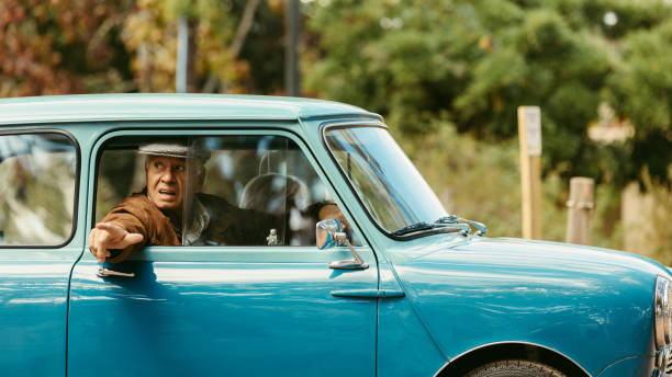 Elderly man driving a car carefully on road. Senior man looking out of the car window and putting his hand out before taking a turn on road.