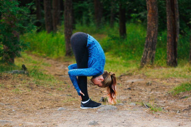 istock Girl in blue sportswear doing exercises outdoors in coniferous forest. Standing forward fold. Healthy lifestyle sport concept. 1020654406