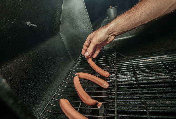 A Man Placing Hot Dogs On A Grill