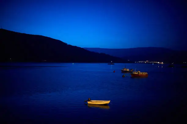 A yellow boat at Fort William at night with dark blue glow from the night sky reflected on the water's surface