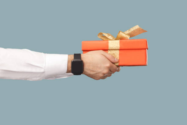 Business people concept, richly and success. human hand in white shirt with black smart watches holding red gift box with gold ribbon. Business people concept, richly and success. human hand in white shirt with black smart watches holding red gift box with gold ribbon. profile side view. Indoor, studio shot on light blue background pedometer photos stock pictures, royalty-free photos & images