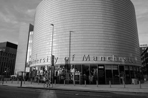 Manchester, United Kingdom - July 25, 2018: A cyclist passes by the large, drum-shaped building of The University of Manchester, University Place, on Oxford Road in Manchester.