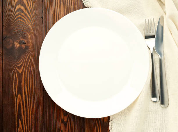 istock Blank flat gray plate, fork, knife on dark brown wooden table, top view. Mock up, copy space, concept restaurant 1020756026