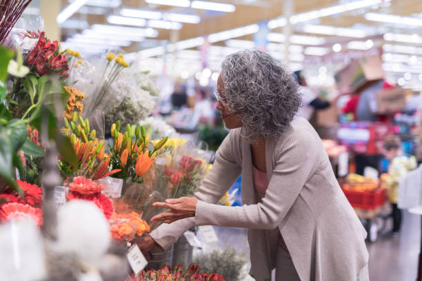 年配の女性が店で花をピックアップします。 - florist supermarket flower bouquet ストックフォトと画像