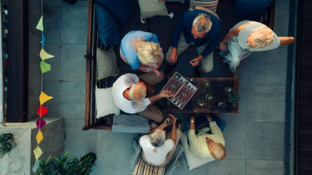 Senior Friends Playing Backgammon Top view of group of senior friends having party on rooftop terrace and playing backgammon together. backgammon stock pictures, royalty-free photos & images