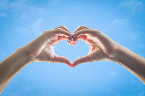 Heart shape woman hands against blue sky background
