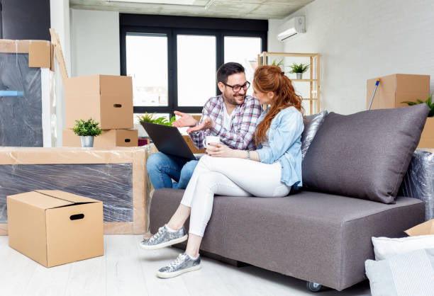 istock Young couple in new home with notebook sitting on sofa and planning with unpacked boxes in background 1020940042