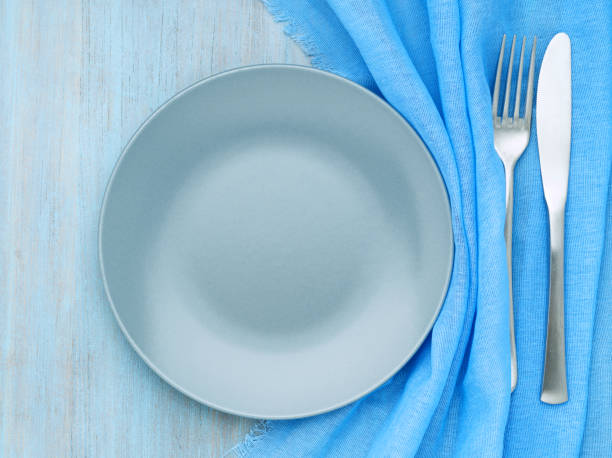 istock Blank flat gray plate, fork, knife on blue wooden table, top view. Mock up, concept for marine restaurant, fish menu 1020952684
