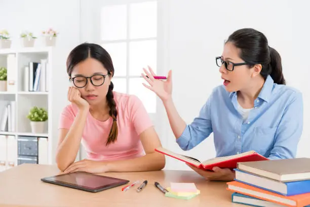 unhappy young individual tutor woman finding female student sleeping during study time and feeling angry.