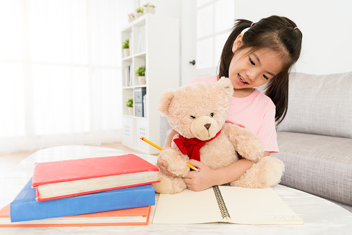 happy pretty little girl teaching teddy bear doing school homework.