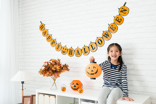 happy kids holding a pumpkin lantern and sitting on the cabinet of the living room after help her family to decorating