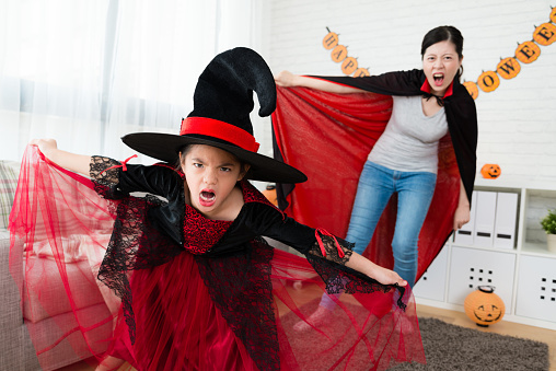 horror little witch girl wear a hat with her mother wearing vampire cloak try to scare people