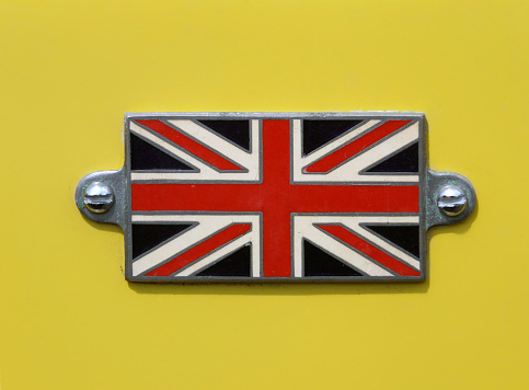 A Vintage British Union Jack flag metal badge on a yellow car close up