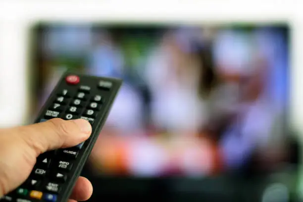Hand with remote control and TV set in the background