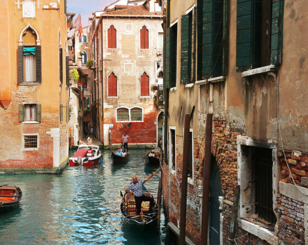 Classic Venetian view with Gondoliers on gondolas with tourists in a small canal surrounded with old buildings stock photo