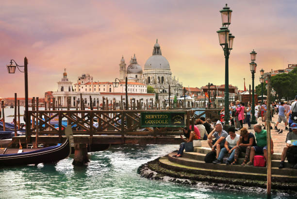 Tourists sitting on the steps near gondolas with Basilica di Santa Maria della Salute in the background stock photo