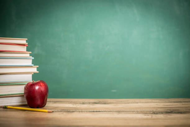 istock Textbooks, apple on wooden school desk with chalkboard. 1021174494