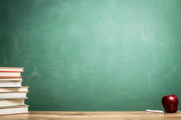 istock Textbooks, apple on wooden school desk with chalkboard. 1021174538