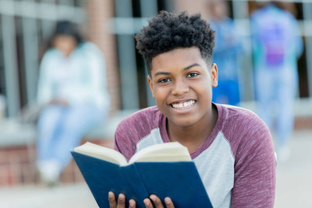 handsome high school boy reads book on campus - adolescence teenager high school student teenagers only imagens e fotografias de stock