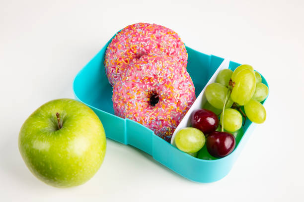 una scatola da pranzo in plastica con ciambelle e uva. mela verde. il concetto di pranzo scolastico. lo sfondo è bianco. - box cake food lunch foto e immagini stock