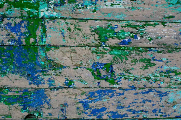 The old building of painted wooden boards with dried green and blue paint on the street in the daylight, the boards parallel to each other, rectangular in shape, create the impress