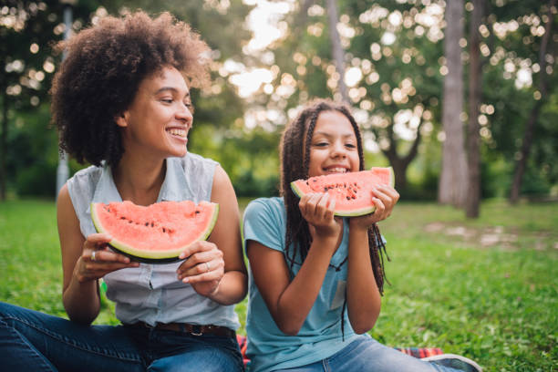 donna felice che tiene l'anguria e guarda la ragazza che mangia una fetta - picnic watermelon summer food foto e immagini stock