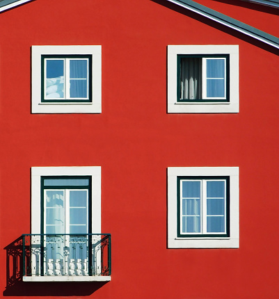 The red facade with three white windows and a balcony door