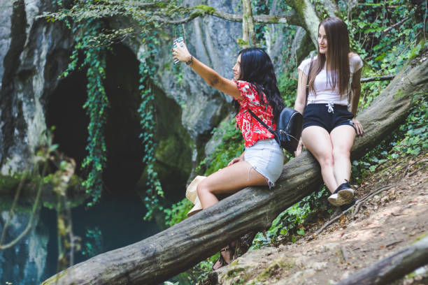 istock Young women sitting on a tree trunk near blue spring in forest 1021240860