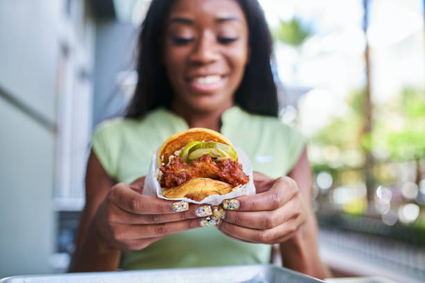 femme afro-américaine tenant le sandwich de poulet frit croustillant style fast-food - chicken sandwich photos et images de collection