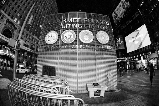New York City, USA - October 11, 2014: Black and white wide angle (16mm fish-eye lens and full frame DSLR camera) view of Times Square by night with illuminated billboards and crowds of people. In the foreground is The U.S. Armed Forces recruiting Station (for the Army, Navy, Air Force and Marines). Times Square is located at the junction of Broadway and Seventh Avenue stretching from West 42nd to West 47th Streets. Times Square is located in the midst of Broadway Theater District and many theatres, restaurants, bars, hotels and shops are situated on Times Square and the surrounding area.