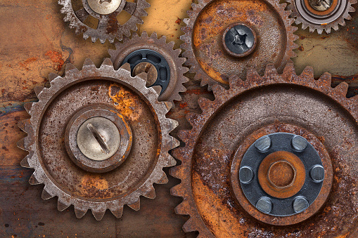 A collection of connected rusty gears over a rusty metal background.