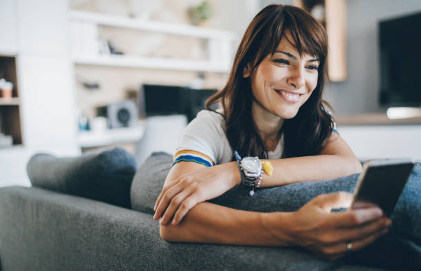 Young woman using smart phone Young bautiful woman texting surfing the net on the sofa at home only mid adult women stock pictures, royalty-free photos & images